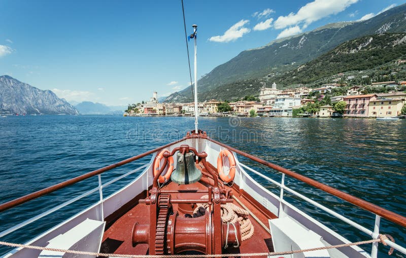 Boat tour: Boat bow, view over azure blue water, village and mountain range. Lago di Garda, Italy