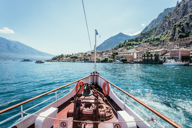 Boat tour: Boat bow, view over azure blue water, village and  mountain range. Lago di Garda, Italy