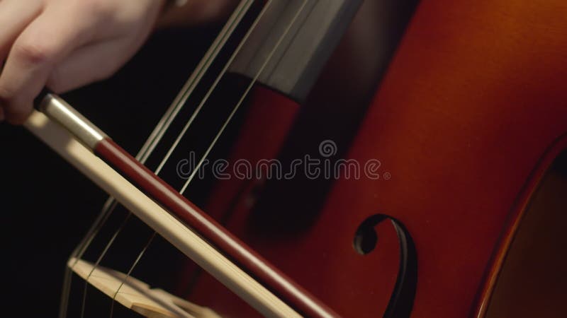 Bow plays on strings of cello reproducing classical music, closeup. Musician plays bow on strings of musical instrument stock footage