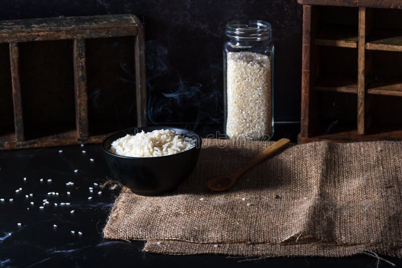 Bowl of Cooked White Rice Smoking and Glass Jar with Uncooked Rice