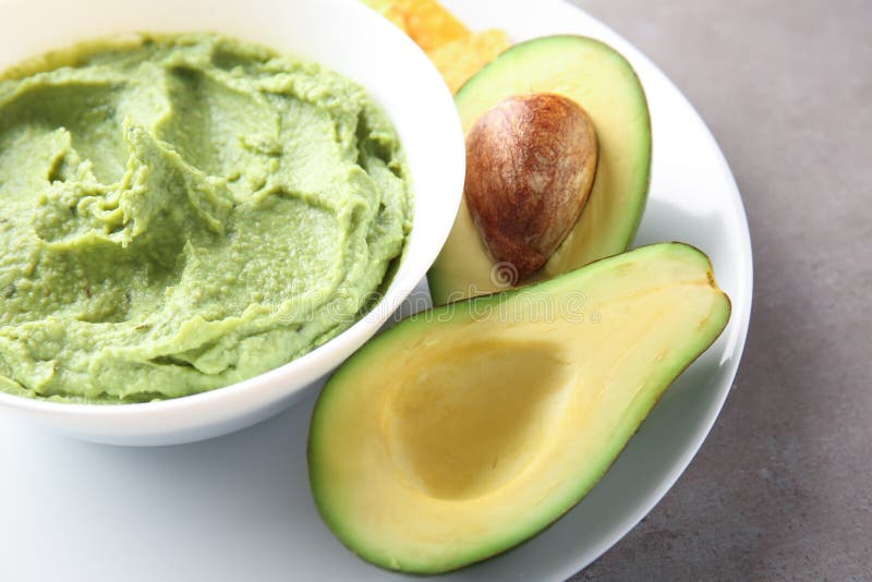 Bowl with delicious guacamole and ripe avocado on plate stock photography