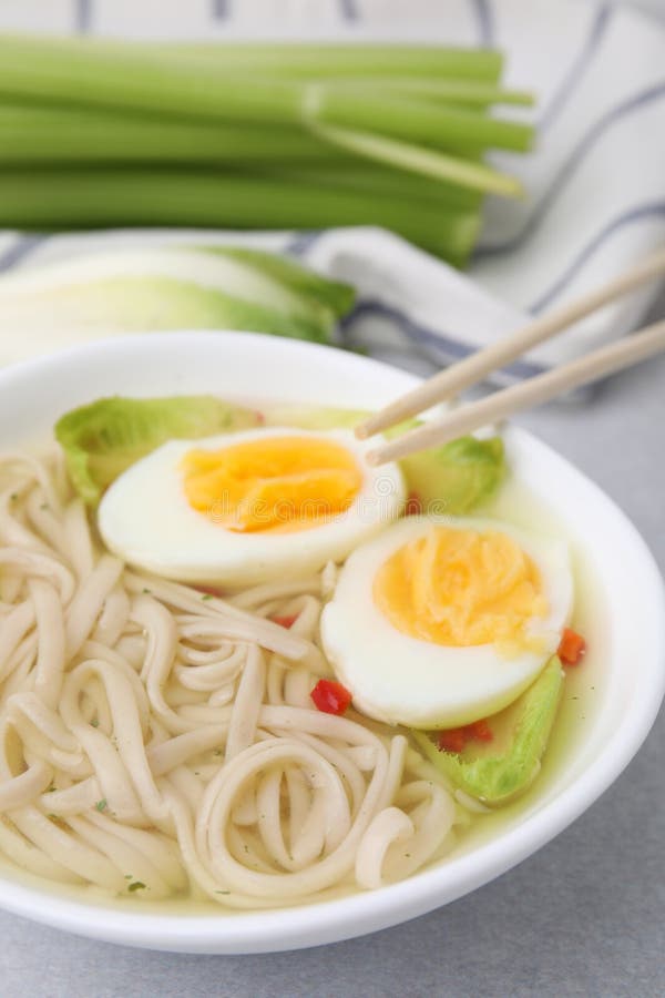 Bowl of Delicious Rice Noodle Soup with Celery and Egg on Light Grey