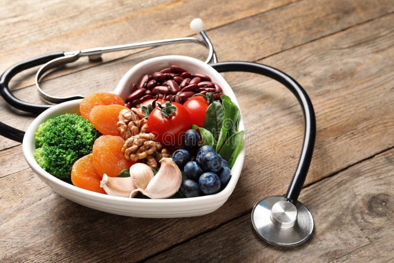 Bowl with heart-healthy diet products and stethoscope on wooden table