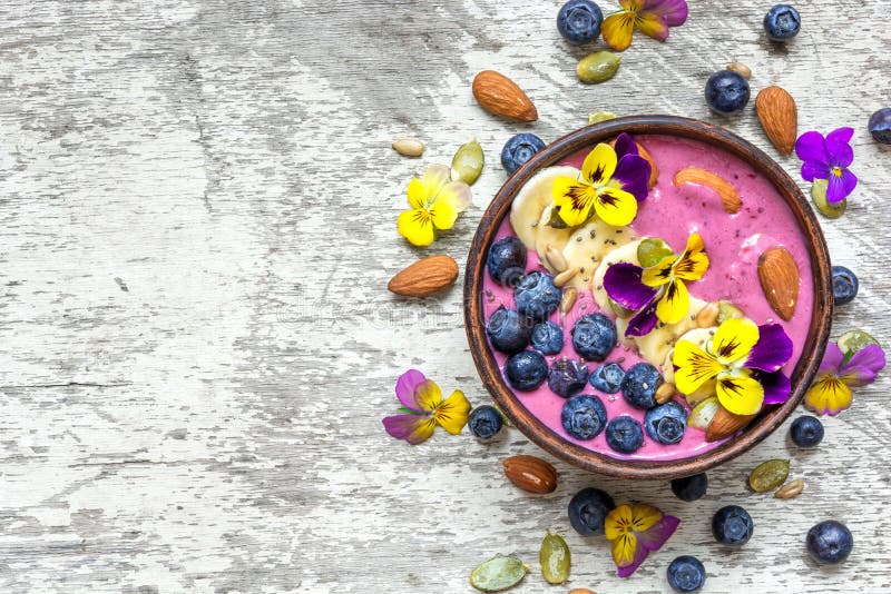 Bowl of homemade smoothie topped with fresh blueberries, nuts, chia and pumpkin seeds and flowers