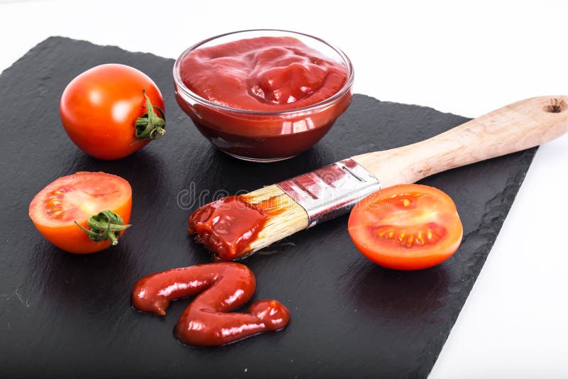 Bowl with ketchup, tomatos and brush on black stone background