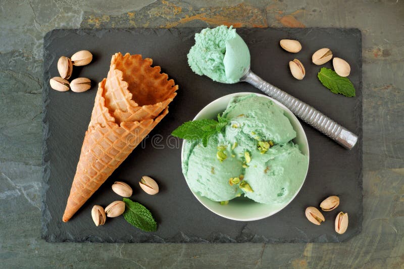 Bowl of pistachio ice cream, above scene with cones on slate