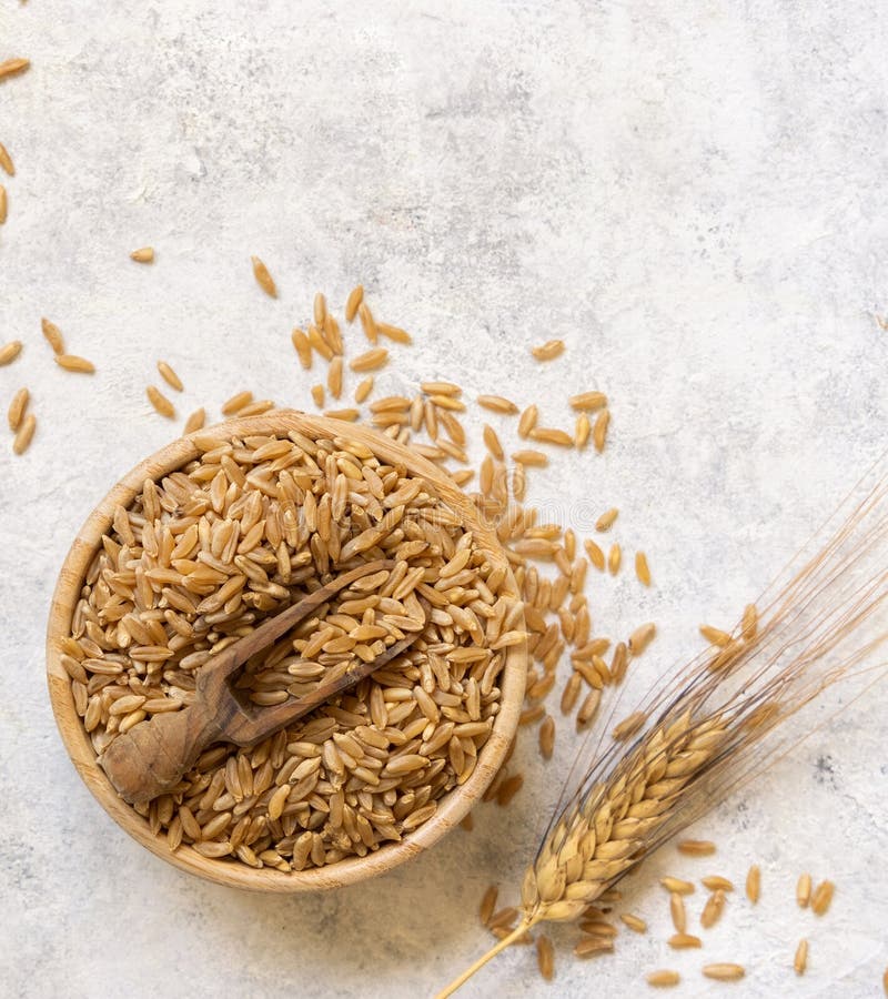 Bowl of Raw Dry Rye Grain with a Wooden Spoon on White Table Top View