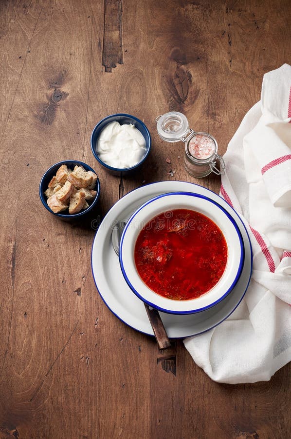 Bowl of red beetroot soup borscht with sour cream and bread crackers on rustic background. Top view with copy space