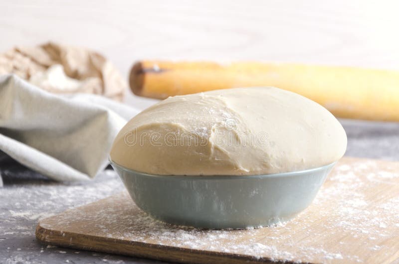 Bowl with risen dough on the cutting brown board,wooden rolling pin,flour in the paper bag as a background.Bread or pizza dough on stock photos Bowl with risen dough on the cutting brown board,wooden rolling pin,flour in the paper bag as a background.Bread or pizza dough on stock photos