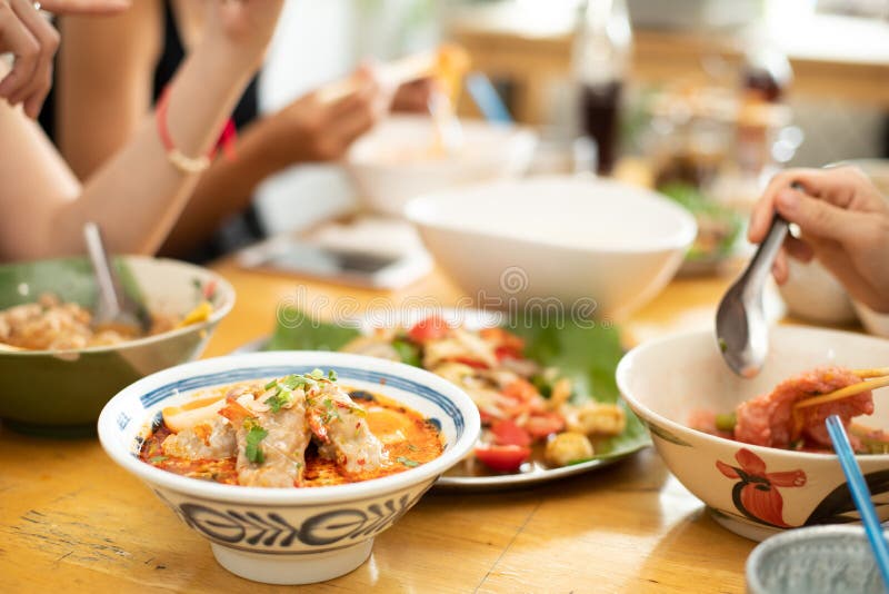 A Bowl of Tomyum Spicy noodle soup with blur background of Friends enjoy eating