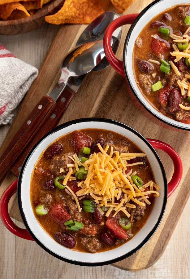 Bowl of chili con carne with shredded ceddar cheese on a rustic wooden table.  Overhead view. Bowl of chili con carne with shredded ceddar cheese on a rustic wooden table.  Overhead view