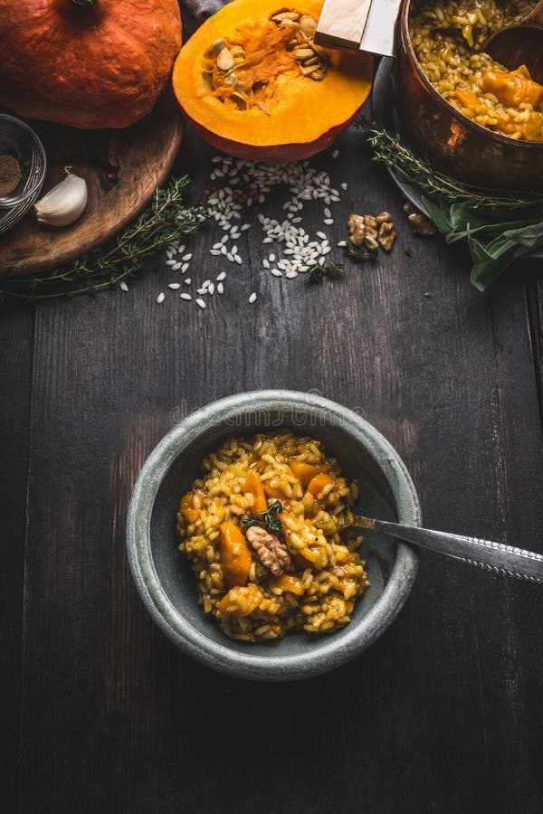 Bowla med vegetarisk den pumparisotto och skeden på mörk lantlig köksbordbakgrund med matlagningingredienser, bästa sikt Sunt arkivfoto Bowla med vegetarisk den pumparisotto och skeden på mörk lantlig köksbordbakgrund med matlagningingredienser, bästa sikt Sunt arkivfoto