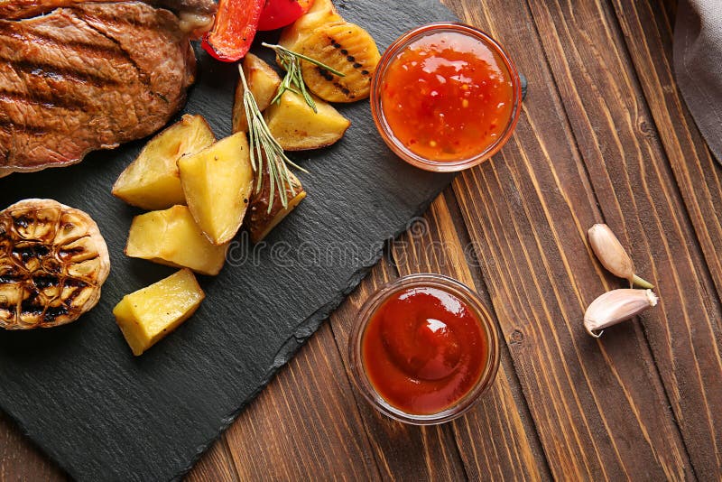 Bowls of barbecue and chili sauce with grilled meat and potato on wooden table stock image Bowls of barbecue and chili sauce with grilled meat and potato on wooden table stock image