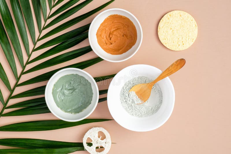 Bowls with clay masks for face treatment with tropical palm leaf on brown background, top view. Facial skincare concept