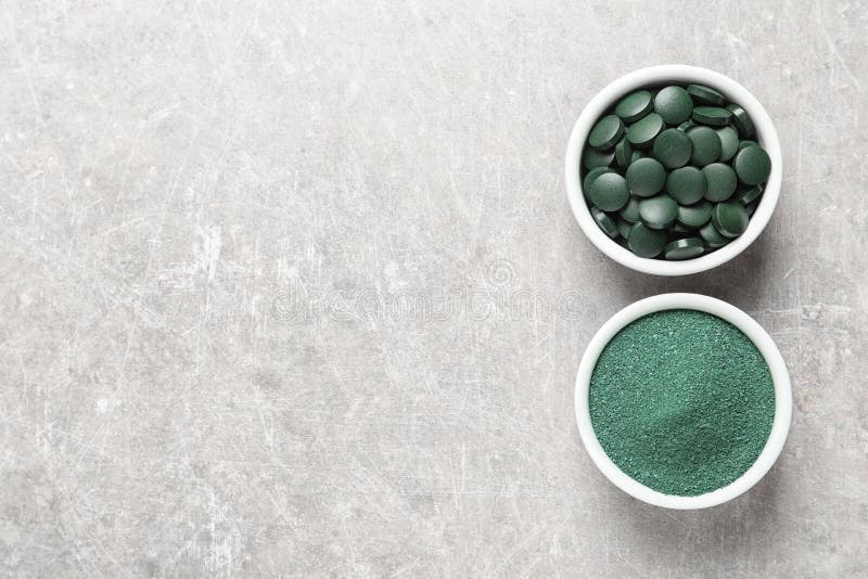 Bowls of spirulina pills and powder on color background, top view.