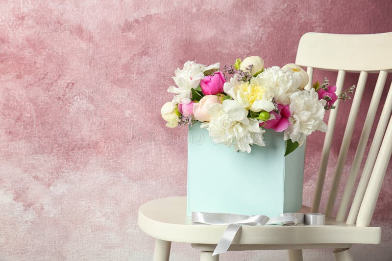 Box with beautiful flowers on wooden chair against color background