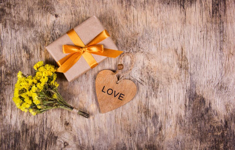 A box with a gold ribbon on an old wooden background. Wooden heart and flowers. Copy space. Flat lay