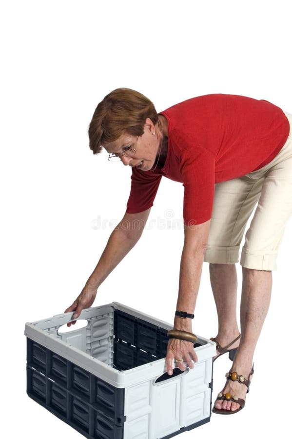 Middle aged woman leaning over to lift a plastic storage box or crate, white studio background. Middle aged woman leaning over to lift a plastic storage box or crate, white studio background.