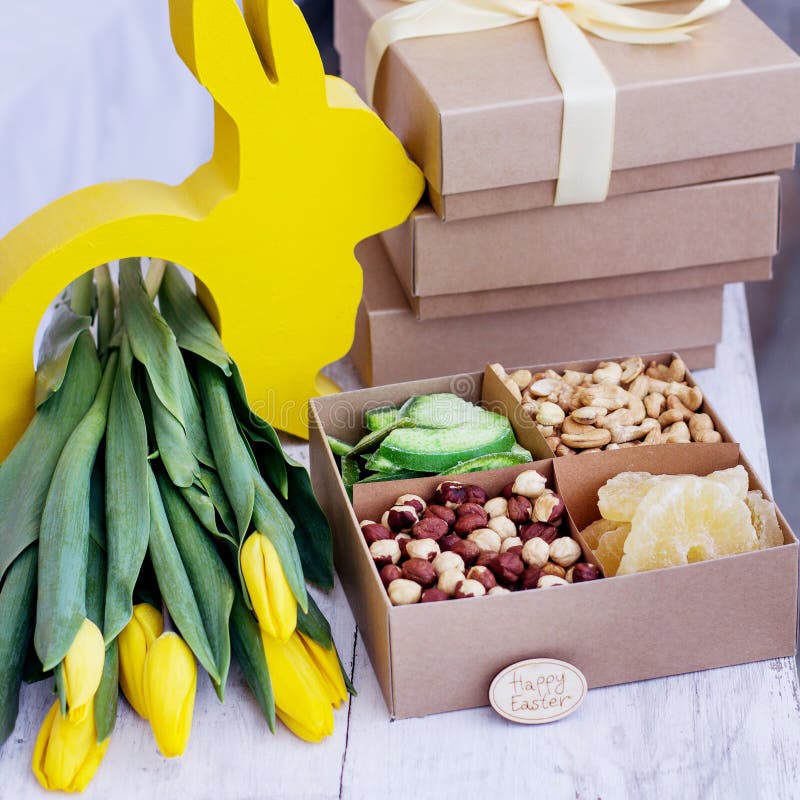 Box with nuts and dried fruits. Easter table. Yellow easter bunny, bouquet of yellow tulips.