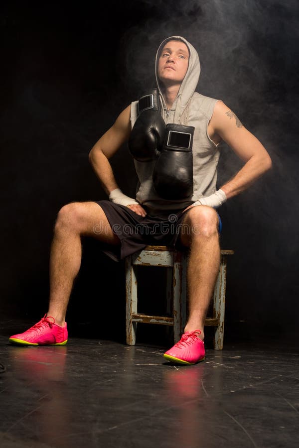 Boxer collecting his concentration before a fight sitting on a stool against a darkmbackground with his gloves around his neck and eyes closed