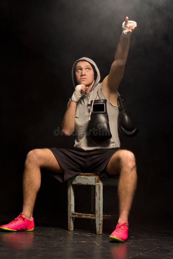 Boxer sitting waiting on a wooden stool in a darkened corner pointing to heaven as he psyches himself up before a fight asking for help to win the match. Boxer sitting waiting on a wooden stool in a darkened corner pointing to heaven as he psyches himself up before a fight asking for help to win the match.