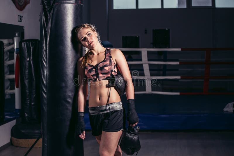 Boxeur de femme se penchant en avant au repos sur un sac de sable énorme images stock Boxeur de femme se penchant en avant au repos sur un sac de sable énorme images stock