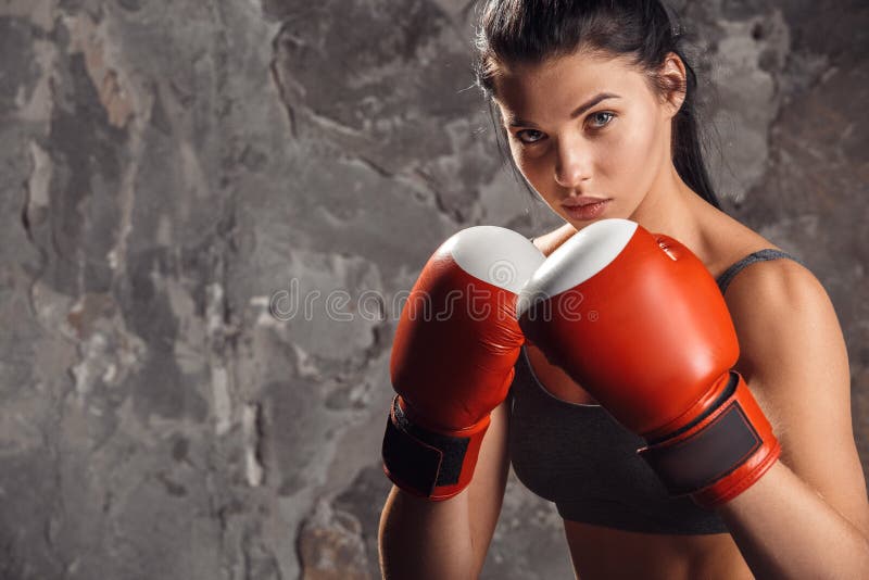 Boxing. Woman boxer in gloves standing isolated on wall ready to kick confident.