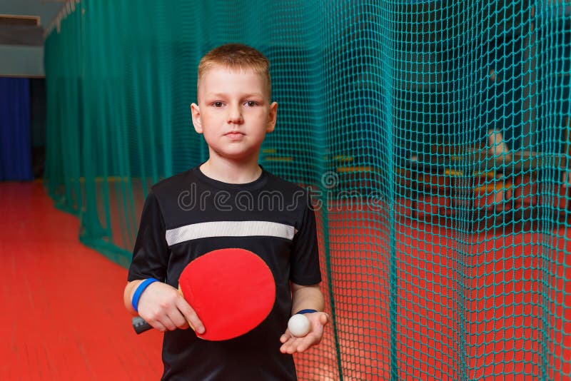 Boy in a black T-shirt holds a racket and a table tennis ball