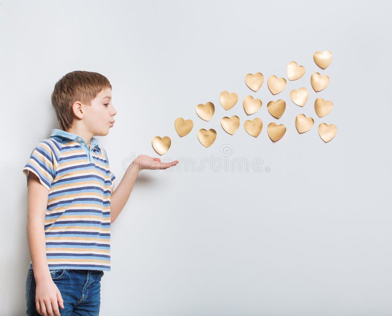 Boy blowing golden hearts from hand over light grey background