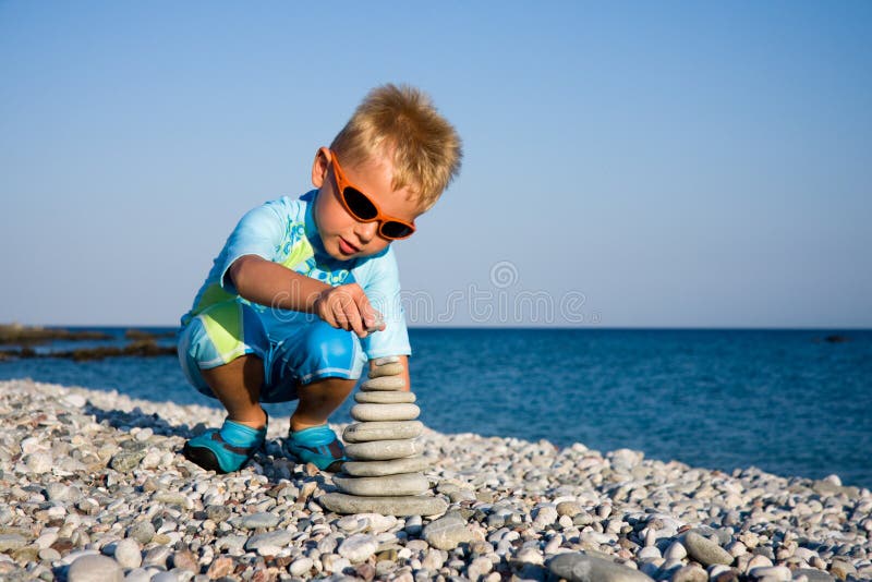 Boy in swim suit building stone stack on pebble beach. Boy in swim suit building stone stack on pebble beach