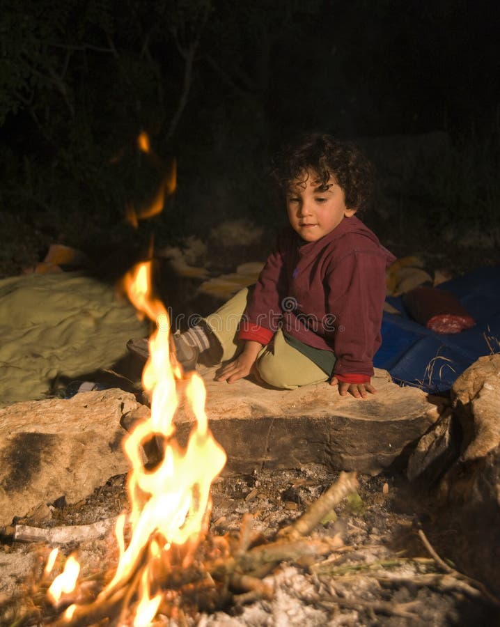 Ragazzo seduto vicino al fuoco in un campo.