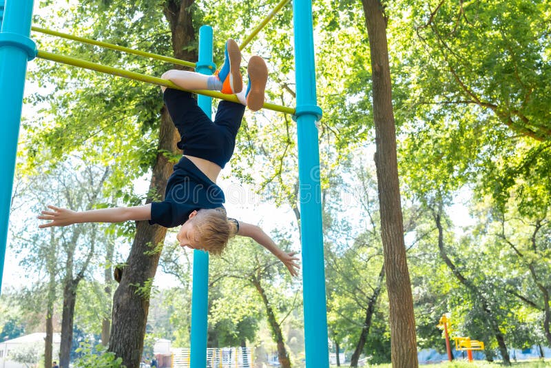 The Boy Caught His Feet on the Horizontal Bar and Hangs Upside Down he