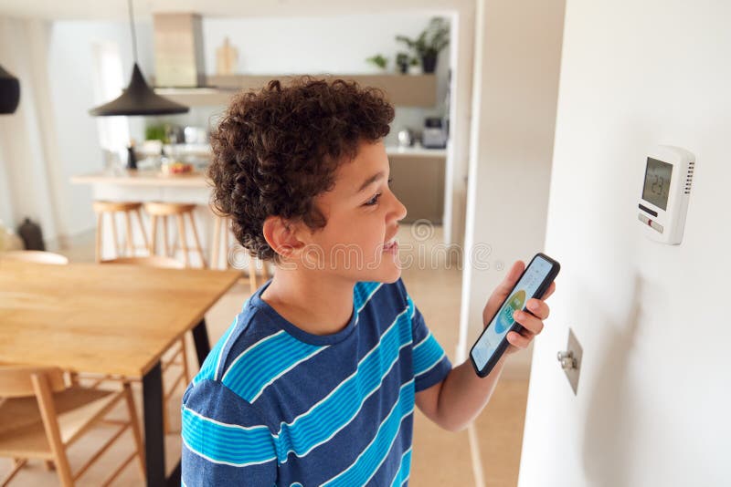 Boy Changes Temperature On Central Heating Thermostat Control Using Mobile Phone App stock photography