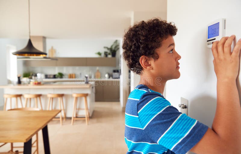 Boy Changes Temperature On Central Heating Thermostat Control Using Mobile Phone App royalty free stock images