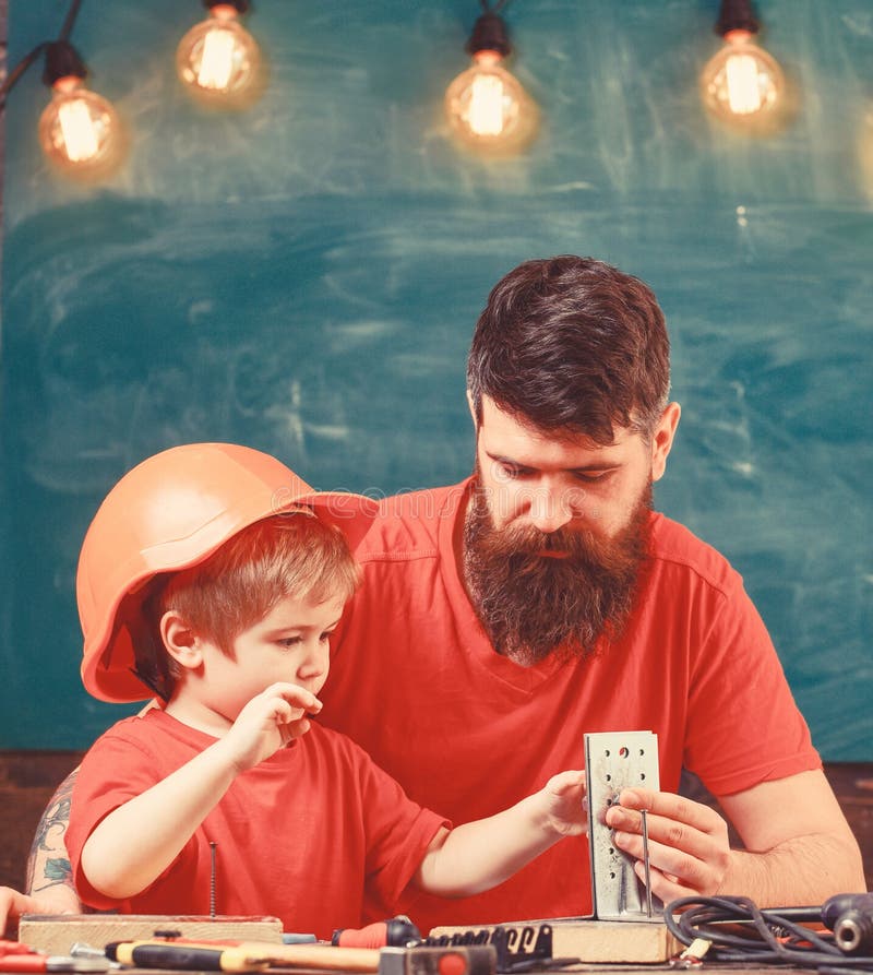 Boy, child busy in protective helmet makes by hand, repairing with dad. Fathers assistant concept. Father with beard.