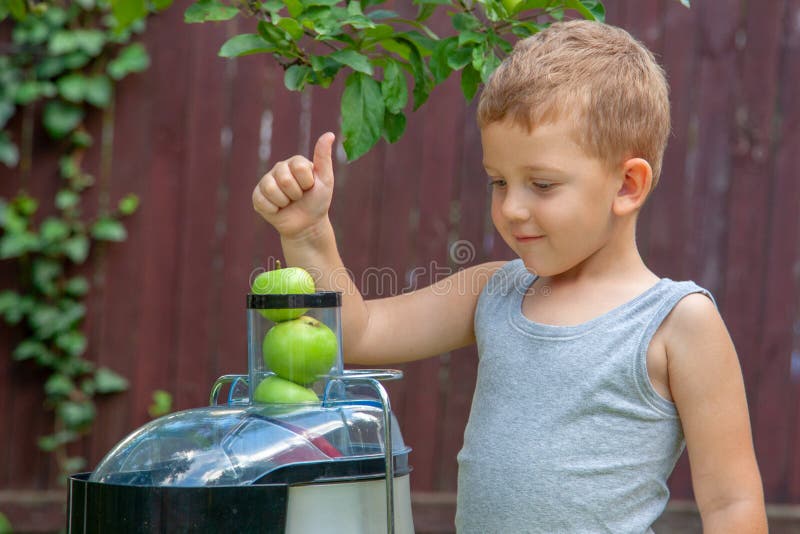 Boy Child Makes Juice from Green Apples in Juicer Outdoors Stock Image