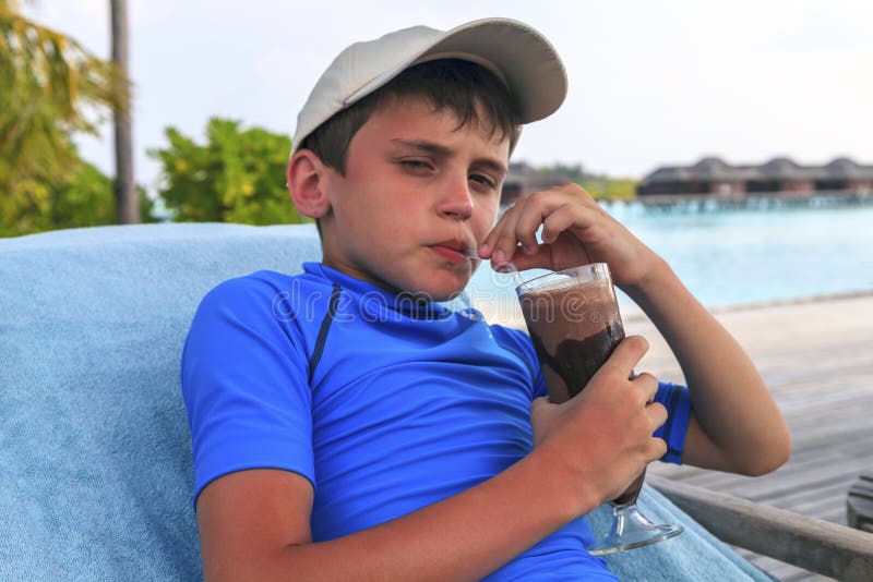 The boy is drinking a chocolate cocktail, lying on a lounger royalty free stock photography