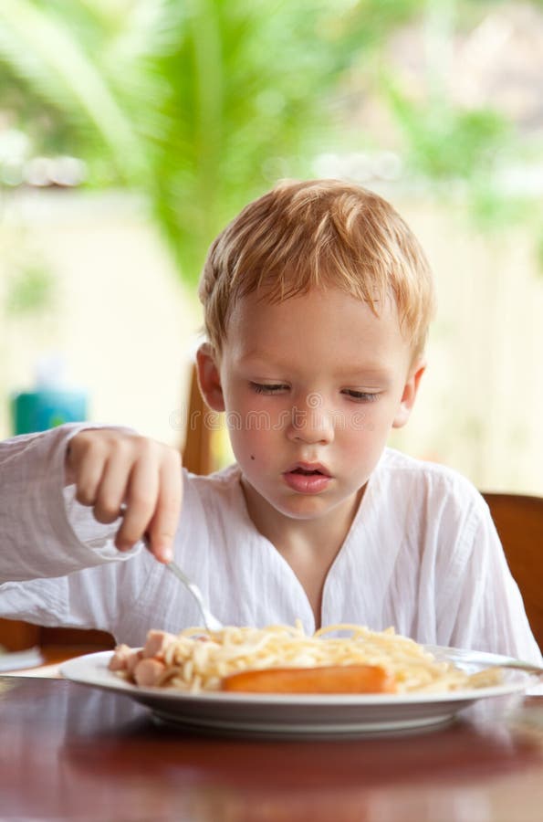 Boy eating spaghetti with sausages outdoors