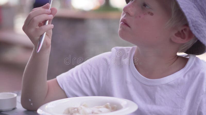 The boy eats vareniki at a table in a cafe