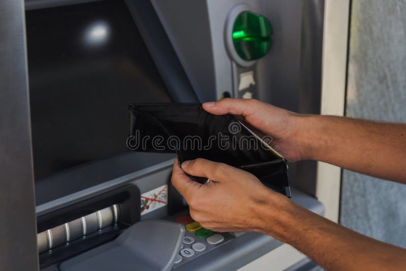 Man holding empty wallet near ATM machine. Concept of being broke