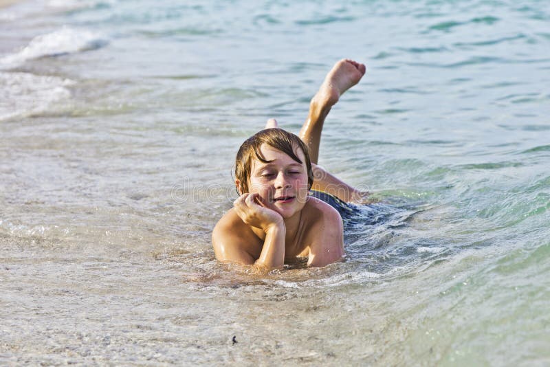 Boy enjoys lying at the beach in the surf