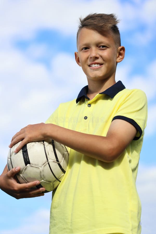 Boy football player in a yellow t-shirt holds the ball in his hands. against the sky