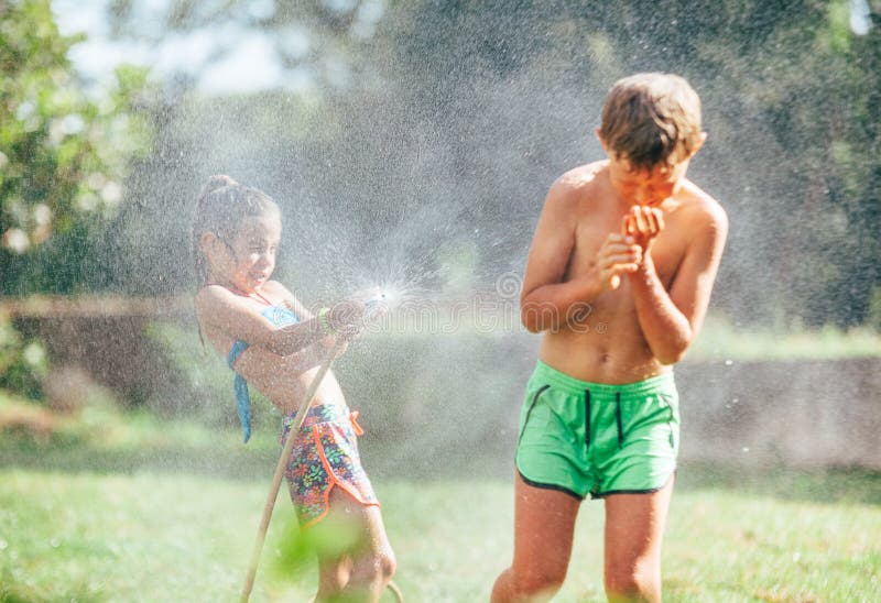 Boy and girl playing in garden, pouring with water each other from the hose, making a rain. Happy childhood concept image