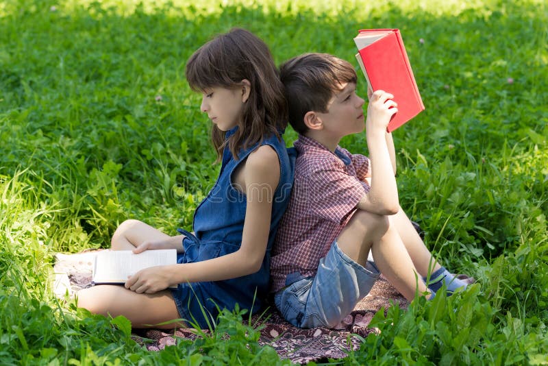 Boy and girl are sitting back-to-back on the lawn in the park and reading books. stock images Boy and girl are sitting back-to-back on the lawn in the park and reading books. stock images
