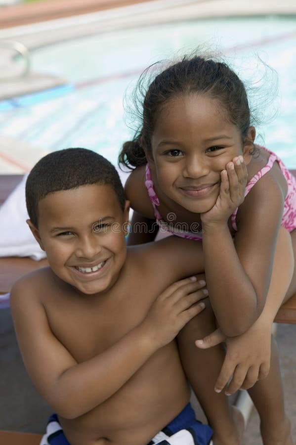 Boy (7-9) and girl (5-6) sitting by swimming pool portrait.