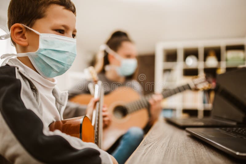 A boy wearing a face mask plays ukulele in front of a laptop Stock