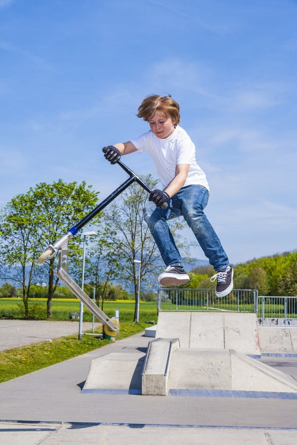 Boy Has Fun Jumping with the Push Scooter at the Skate Park Stock Image