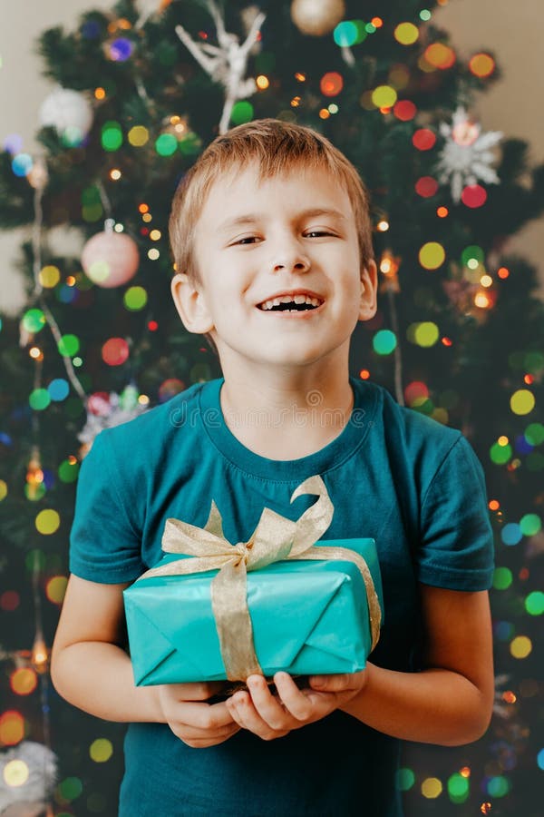 Boy holding blue gift box. Decorated Christmas tree on background