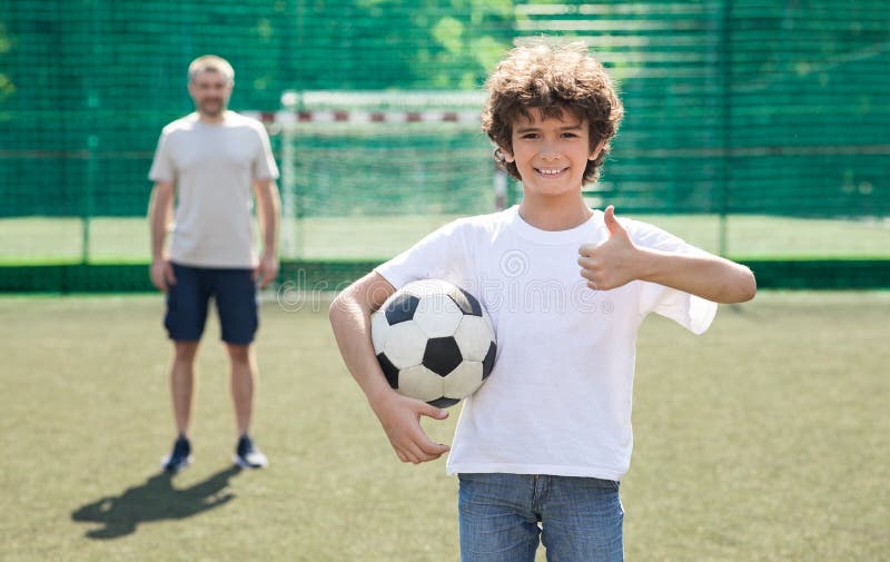 Boy holding soccer ball on the field, showing thumbs up