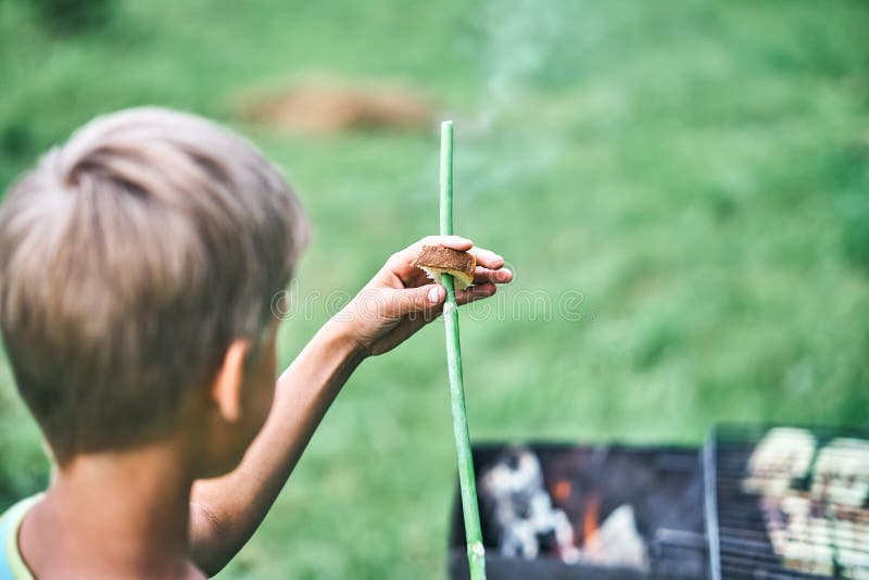 Boy holds smoking green stick near grill with cooking meat royalty free stock photos